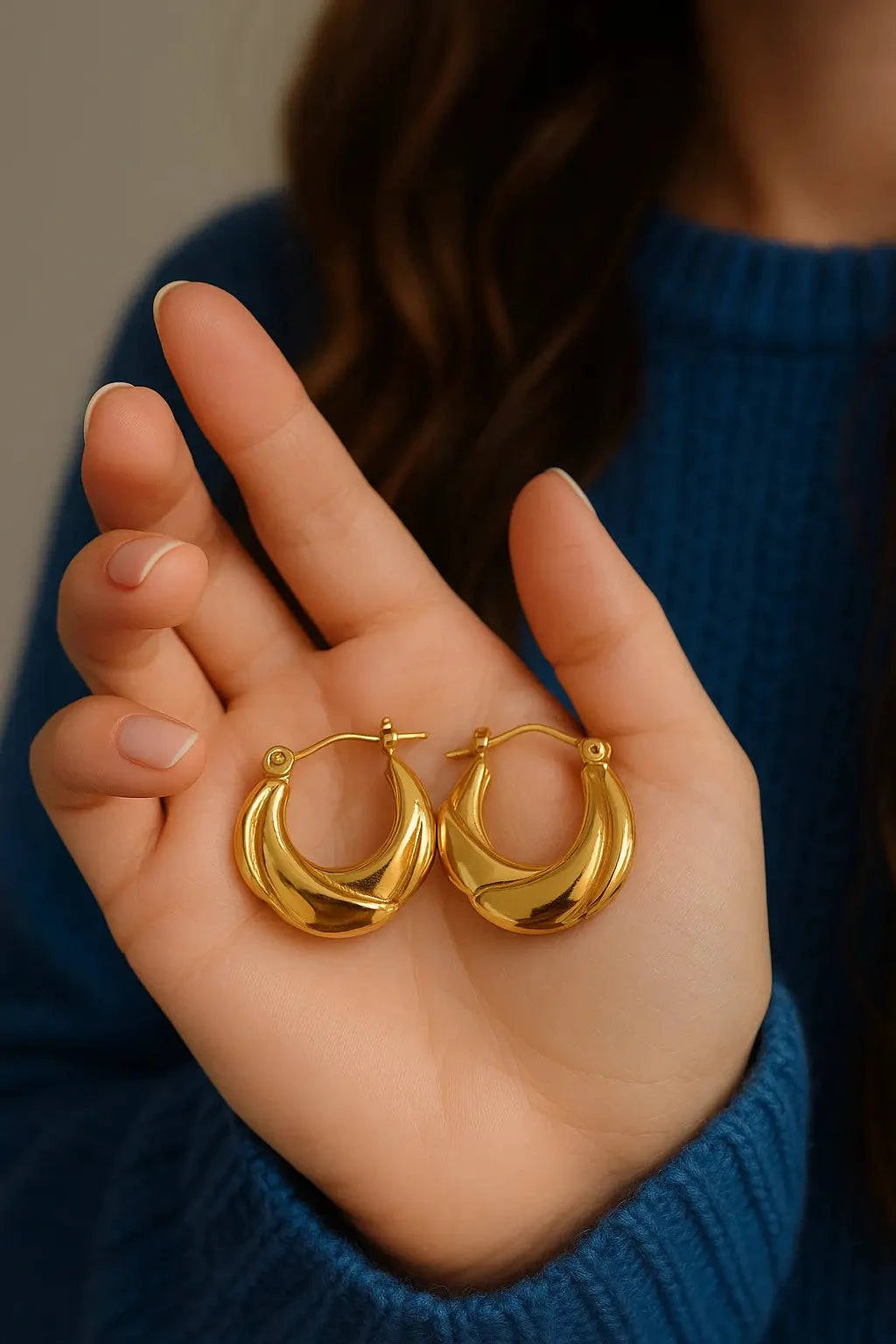 Gold hoop earrings held in a hand with a blurred background