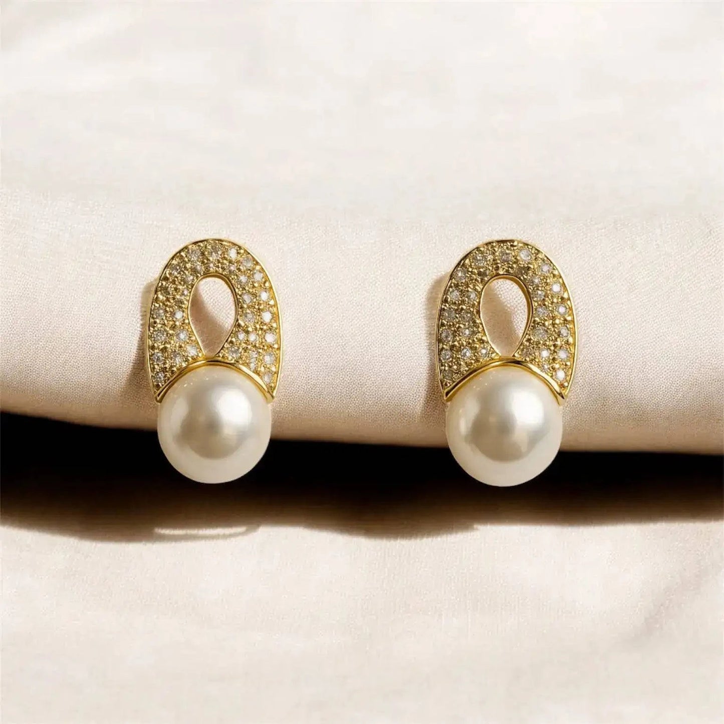 Pair of pearl earrings with gold and diamond accents on a beige surface