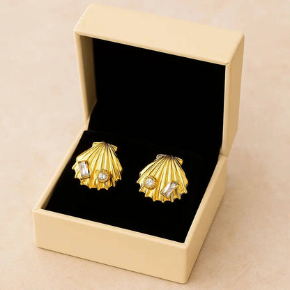 Gold shell-shaped earrings with gemstones in a beige box on a beige background