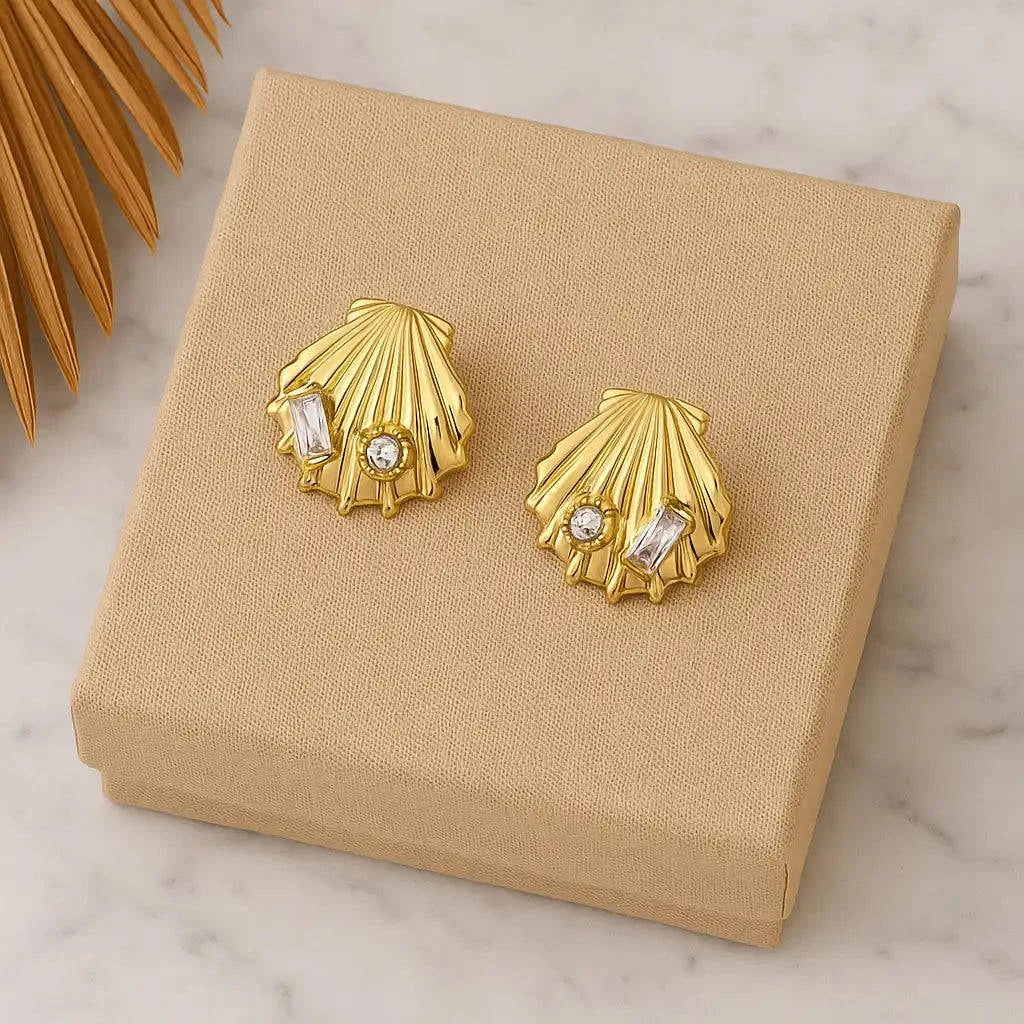 Gold shell-shaped earrings with embedded stones on a beige jewelry box.