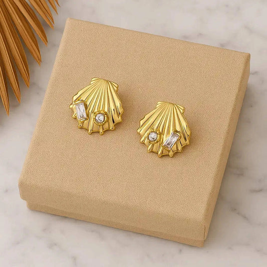 Gold shell-shaped earrings with embedded stones on a beige jewelry box.