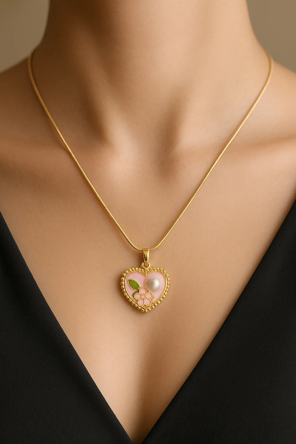 Gold necklace with a heart-shaped pendant featuring a pearl and green leaves on a mannequin.