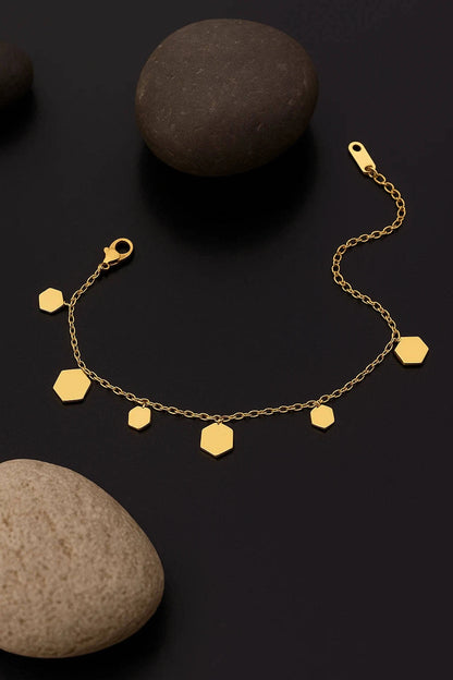 Gold bracelet with hexagonal charms on a dark surface with stones.