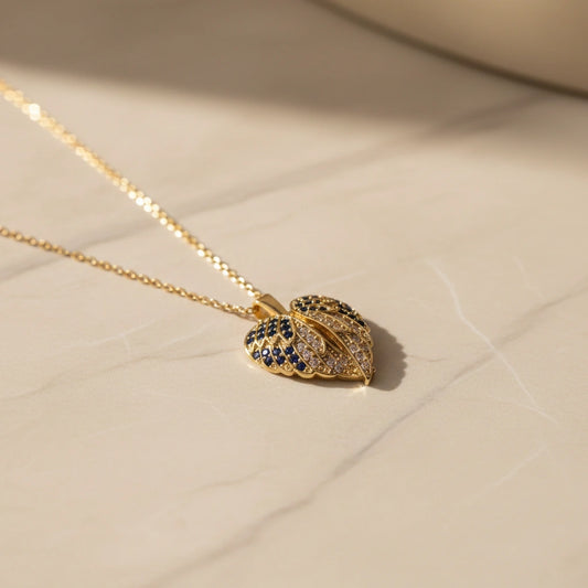 Gold necklace with a leaf-shaped pendant on a beige surface